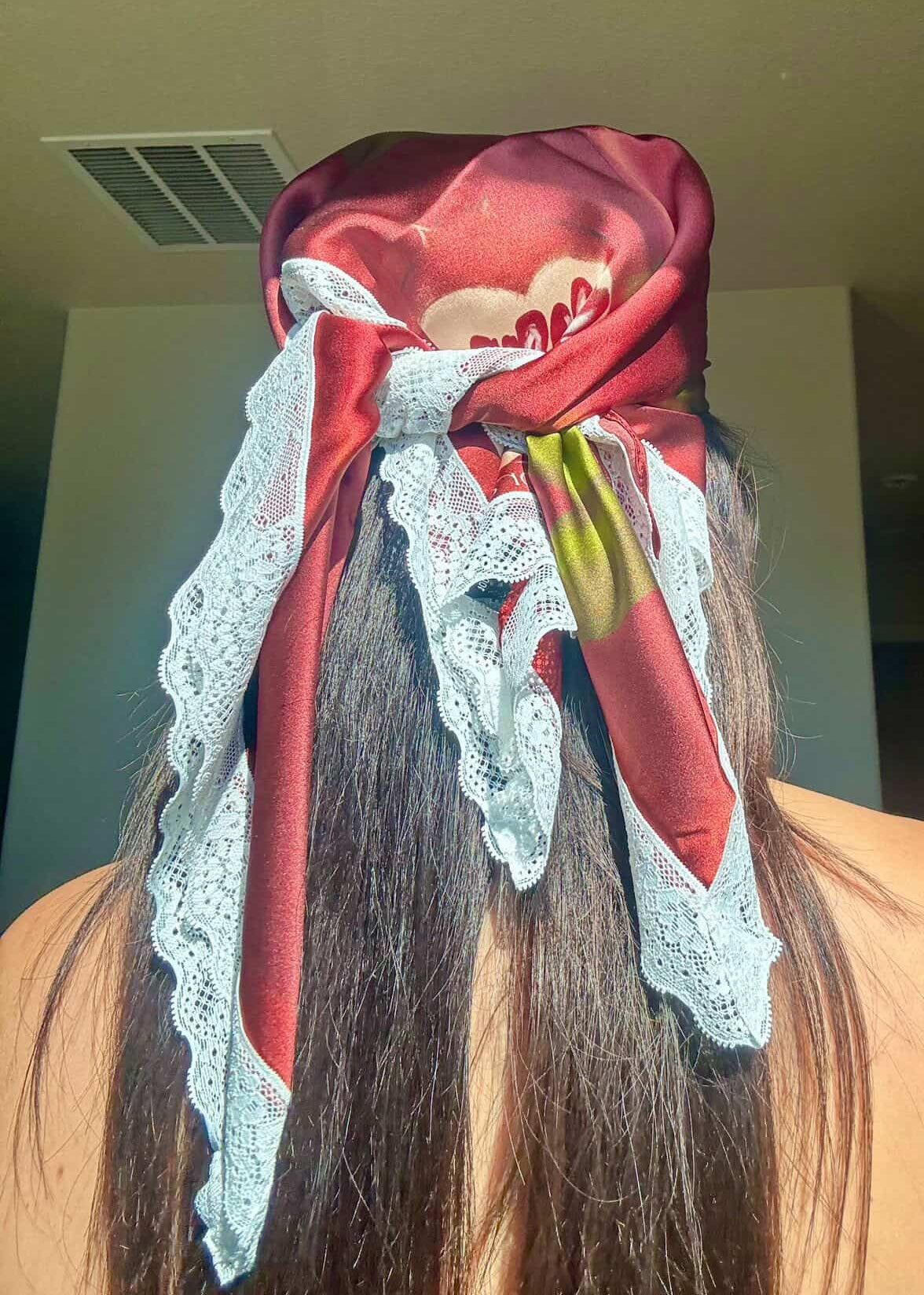 Person wearing a red headscarf with lace details on a plain background