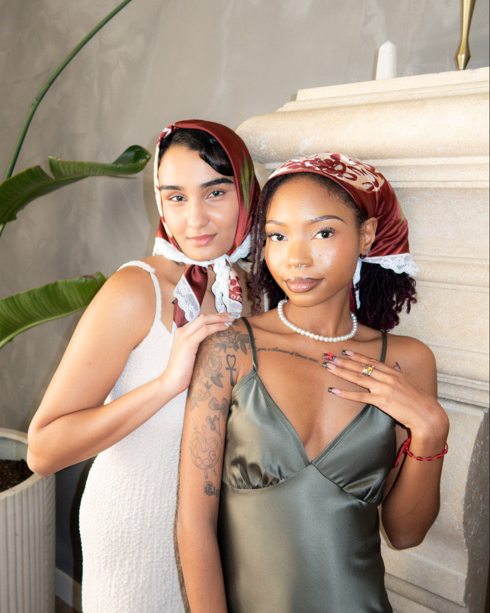 Two women standing on a staircase wearing matching headscarves and satin dresses.