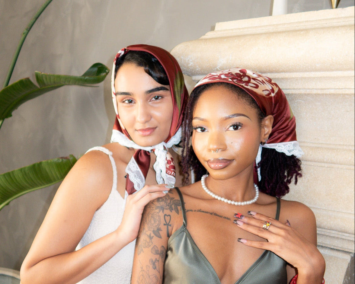 Two women standing on a staircase wearing matching headscarves and satin dresses.
