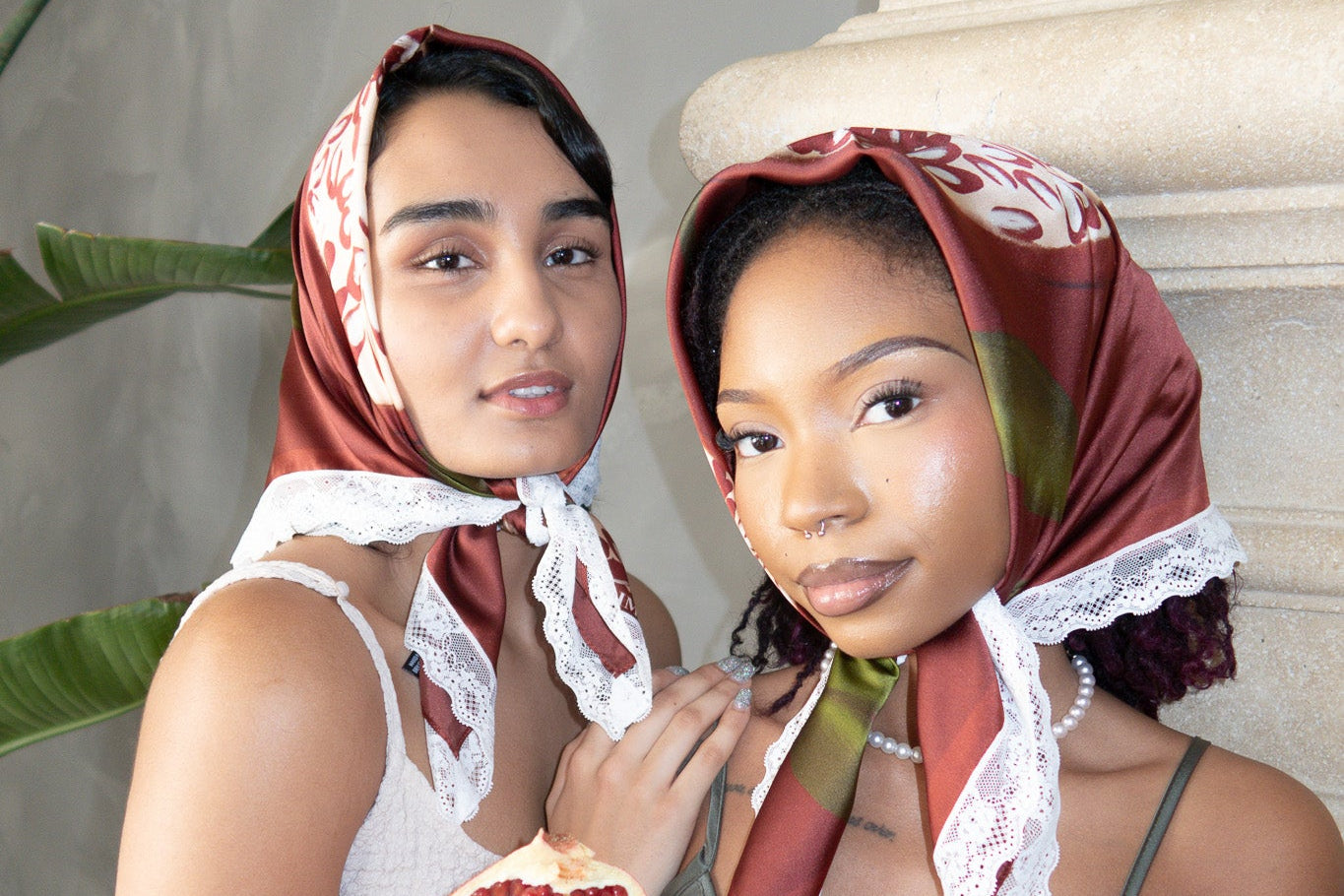 Two women wearing headscarves holding a pomegranate in a decorative setting.