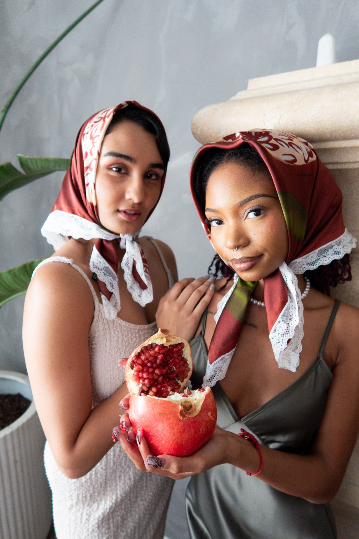 Two women wearing headscarves holding a pomegranate together.