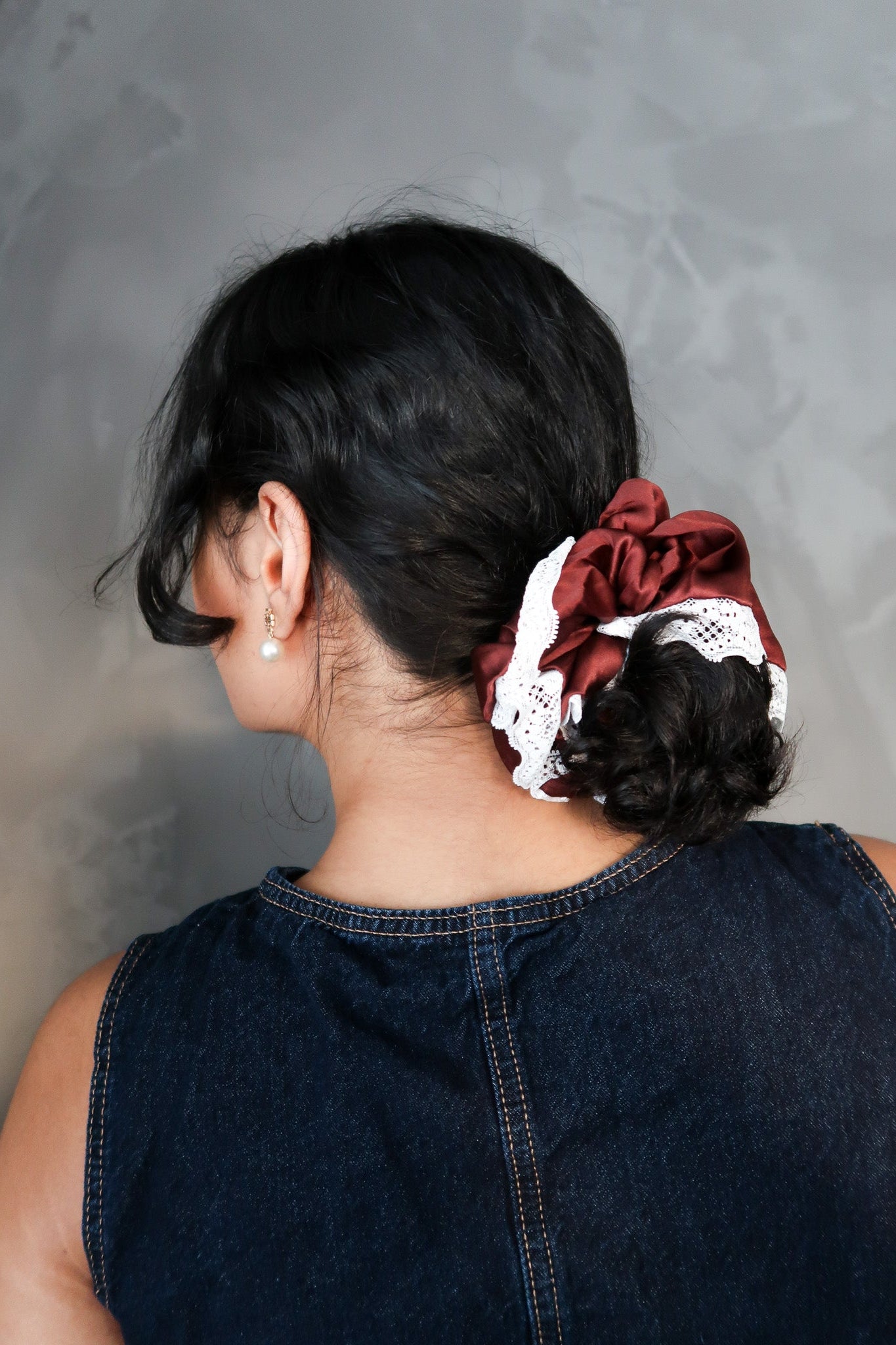 Person with a decorative hair scrunchie in their hair against a gray background