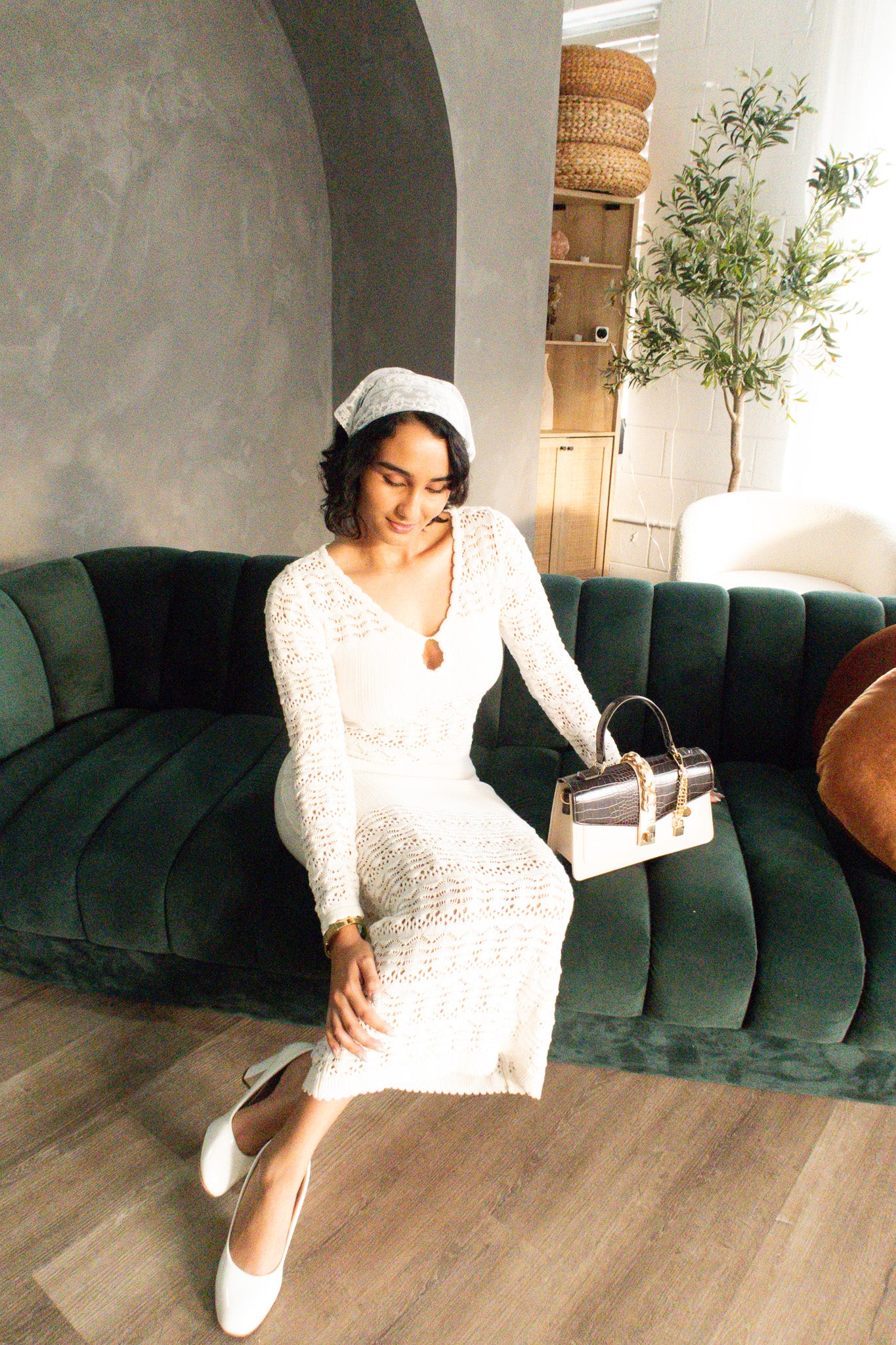 Woman in a white dress sitting on a green couch in a room with a plant and wicker basket.