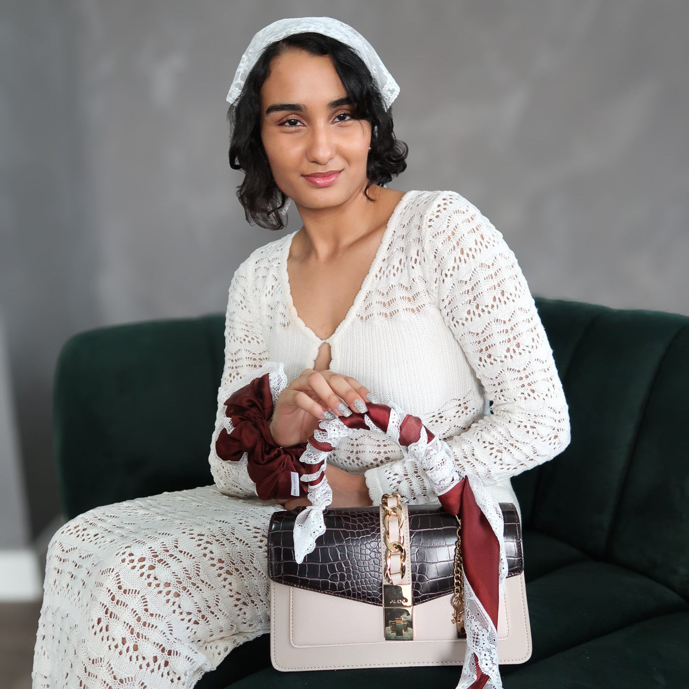 Woman sitting on a couch holding a handbag with a gray background