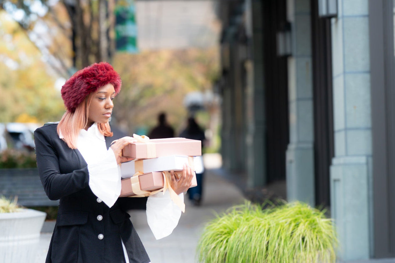 Woman carrying boxes on a city street with a building and plants in the background